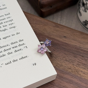 Nahaufnahme eines floralen Zirkonia-Rings mit lila Blütenblättern auf einem alten Buch