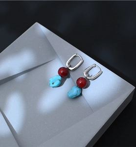 Detail of silver drop earrings with red agate bead and irregular turquoise stone on grey block