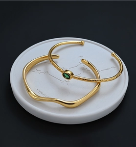 Close-up of gold open bangles with green gemstone and Virgo star pattern ceramic tray