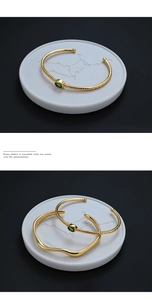 Detail of gold-plated open bangles with green oval gemstone and textured weave finish