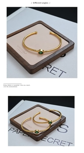 Macro view of gold open cuff bracelet with green gemstone and geometric texture
