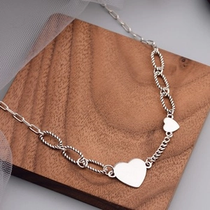 Detail view of silver heart pendants on a textured paperclip link chain with retro vibe