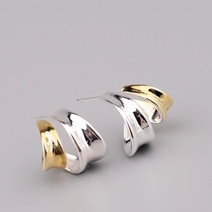 Close-up of twisted C-shaped earrings featuring two-tone gold and silver metallic finish
