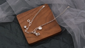 Dettaglio di bracciale argento con ciondoli a stella, orsetto, sorriso e chiusura a moschettone