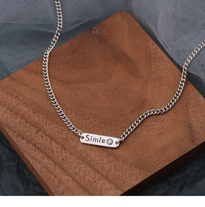 Close-up of a silver Cuban chain necklace featuring a rectangular smile pendant on wood