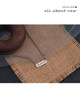 Detailed close-up of a silver smile engraved bar pendant necklace on rustic fabric