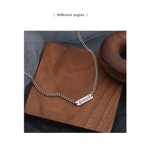 Close-up of a silver smile pendant necklace with engraved rectangular tag on wood