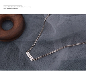 Close-up of S925 silver necklace with long smile tag pendant on blue mesh fabric