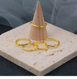 Nahaufnahme minimalistischer Goldringe mit Zirkon auf Stein- und Holzständern