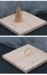 Nahaufnahme eines geometrischen quadratischen Goldrings auf beigem Stein und Holzständer