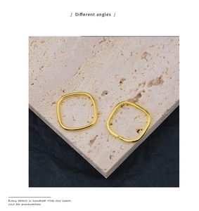 Detail von zwei goldenen quadratischen Creolen aus verschiedenen Winkeln auf Steinfläche
