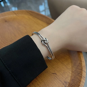 Retro hip-hop style silver intertwined knot open bracelet for women on a wood tray