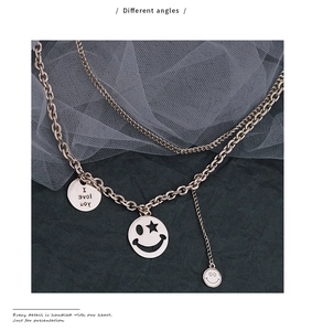Macro detail of rose gold double layer chain necklace with smiley face and engraved charms