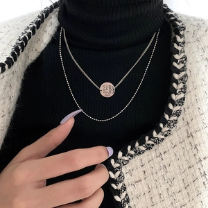 Dual-layer silver necklace with Love You More round pendant on a black knit background