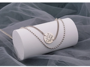 Detail of double-layered silver necklace with Love You More engraved round pendant