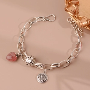 Macro shot of silver-plated chain bracelet with strawberry crystal heart and engraved charms