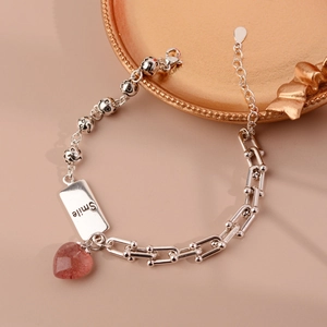Detail of strawberry quartz heart charm on mixed chain bracelet with smile engraving