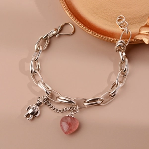 Detail of silver chain bracelet featuring a metal bear and pink heart crystal charm