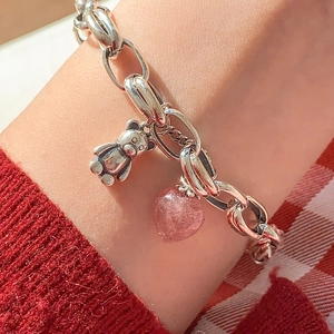 Detailed shot of a silver chain bracelet with a pink heart crystal and teddy bear charm