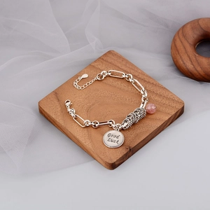 Detail of silver chain bracelet featuring a pink strawberry quartz bead and Good Luck charm