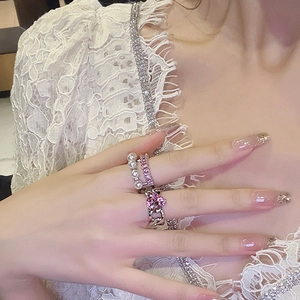 Close-up of pink heart gemstone and pearl rings on a lace fabric background