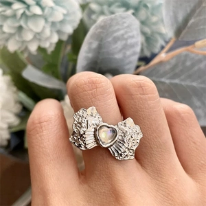 Detail shot of a silver bow ring with a heart-shaped moonstone and vintage textures