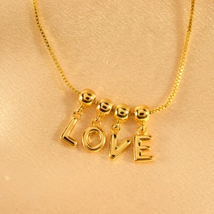 Elegante goldene Box-Halskette mit polierten LOVE-Buchstabenanhängern auf Seidenstoff