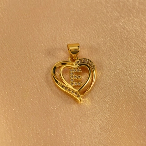 Detail of a golden heart pendant featuring a diamond-encrusted letter E on silk fabric