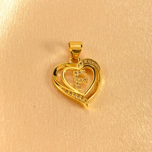 Close-up of gold heart pendant with letter F and sparkling crystals on silk fabric
