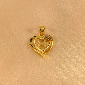 Detailed macro shot of a heart-shaped golden pendant featuring a crystal-studded letter H