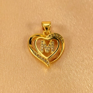 Detail shot of a gold heart-shaped pendant featuring a crystal-paved letter M over satin