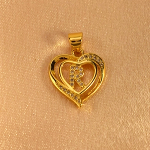 Close-up of heart-shaped gold pendant with cubic zirconia and letter R on silk background