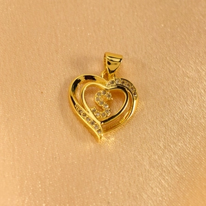 Macro shot of gold heart pendant featuring a micro-paved letter S on luxury silk