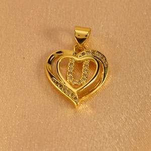 Macro detail of a gold heart pendant with letter U and sparkling white zircons