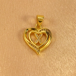 Macro shot of gold heart pendant featuring a sparkling diamond-set letter X detail