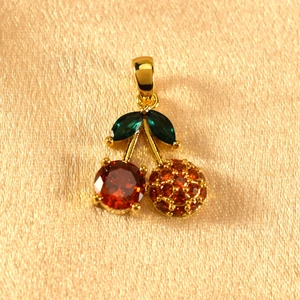 Detailed close-up of cherry pendant with sparkling green leaves and red stones on satin