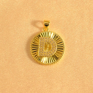 Macro detail of sunburst gold pendant with zircon-encrusted letter D and beaded edge