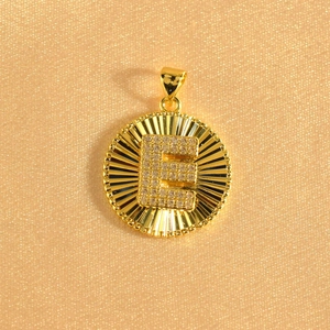 Macro detail of gold-plated sunburst pendant with crystal-encrusted letter E