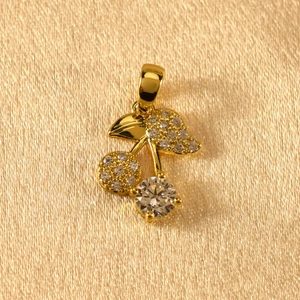 Macro shot of gold cherry pendant with zircon stones on champagne silk background