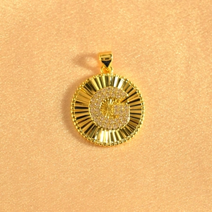 Macro shot of gold-plated sunburst pendant featuring an iced-out crystal pavé letter G
