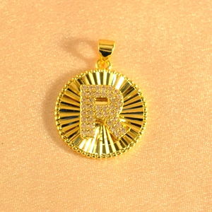 Detailed close-up of a gold-plated sunburst round pendant with crystal encrusted letter R
