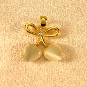Detailed shot of gold bow cherry pendant with heart-shaped cat-eye stones on champagne satin