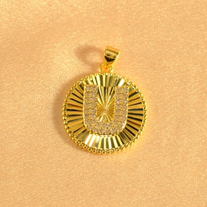 Macro view of gold pendant with letter U diamond setting and sunburst texture