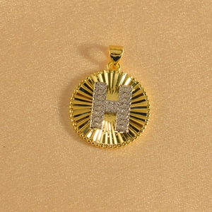 Close-up of gold sunburst pendant with crystal-encrusted letter H on champagne velvet
