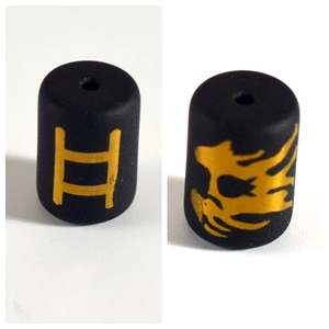 Macro shot of black cylindrical beads with golden zodiac and skull patterns for DIY jewelry
