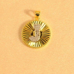 Macro shot of silver paved letter J on a gold sunburst pendant with beaded edges