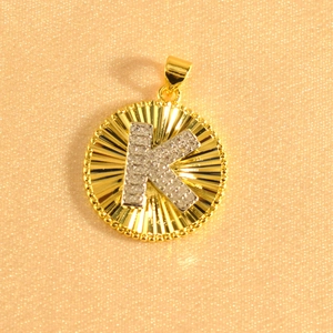Macro shot of gold sunburst pendant with crystal-encrusted letter K and textured details