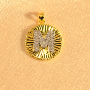 Detail view of gold-plated sunburst pendant with crystal-encrusted letter M charm