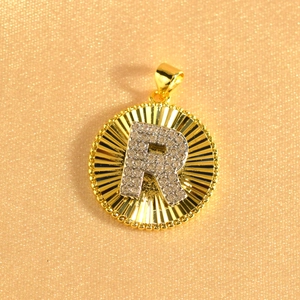 Macro detail of gold plated letter R pendant with radiant sunburst texture and zircons