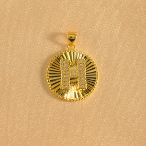 Macro detail of sunburst gold pendant with stone-encrusted H letter and beaded edge
